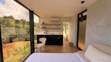 Une chambre moderne avec un grand lit, une vue sur l’extérieur, un petit coin cuisine et un fauteuil.