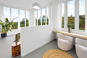 A modern room with large windows, a potted plant, a wooden side table, and a round woven rug.