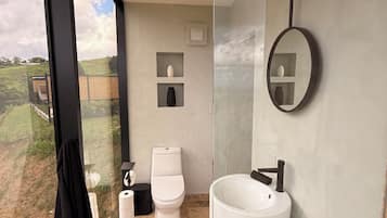 Een moderne badkamer met een groot raam, een wit toilet, een witte wastafel en een zwarte handdoek.