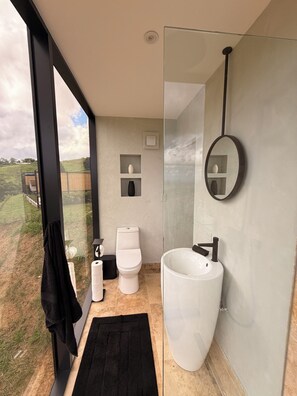 A modern bathroom with a large window, a white toilet, a white sink, and a black towel.