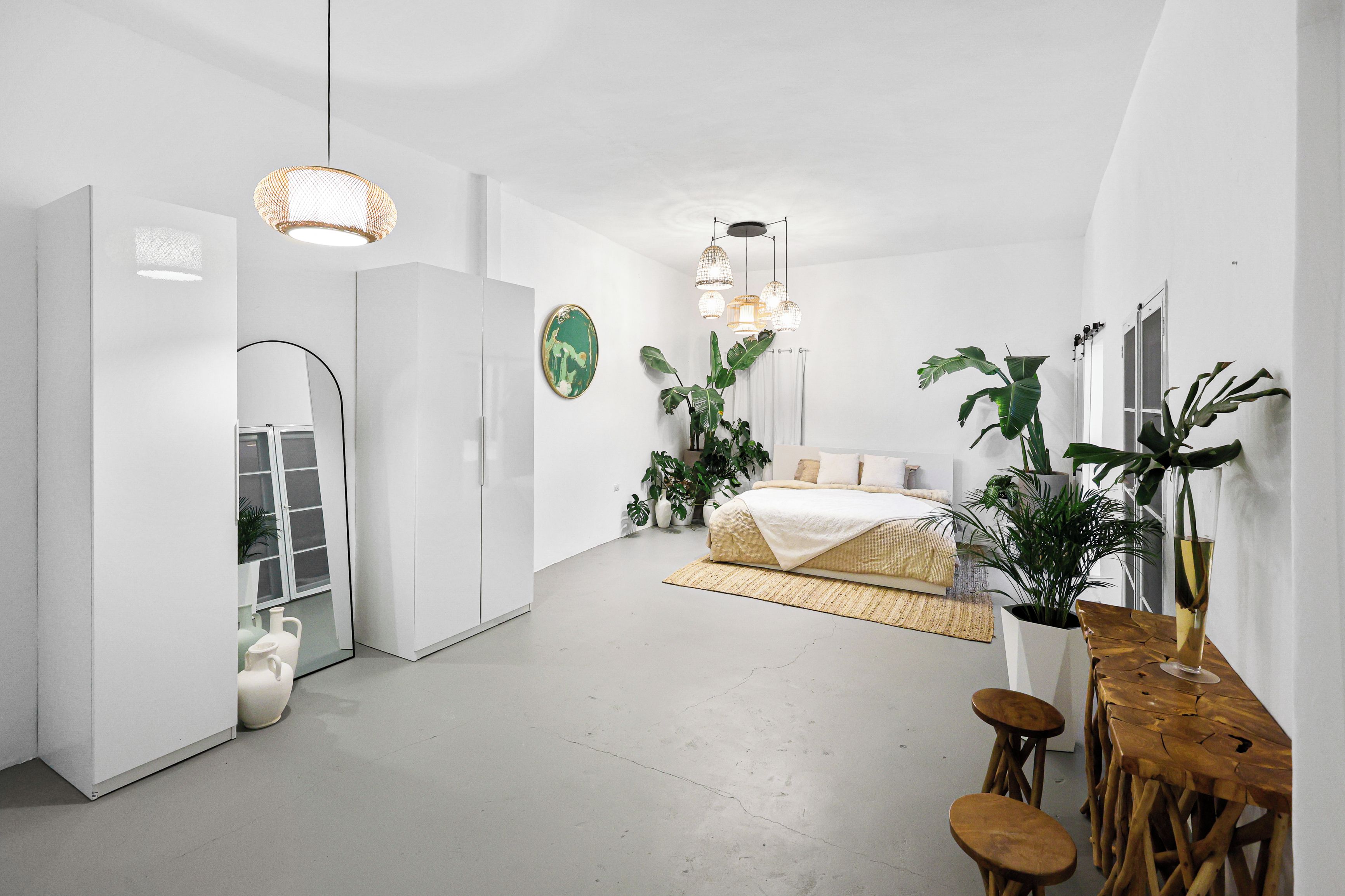 Une chambre à coucher moderne avec un lit, des tables de chevet, un miroir et des plantes en pot.