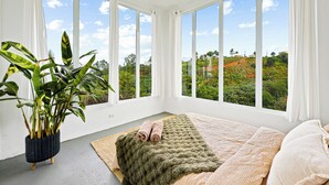 Ein Zimmer mit großen Fenstern, einem Bett mit grüner Decke und einer Topfpflanze.