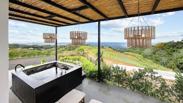 Ein Whirlpool mit Holzverkleidung, zwei hängende Korbstühle und Blick auf einen angelegten Garten sowie entfernte Hügel.