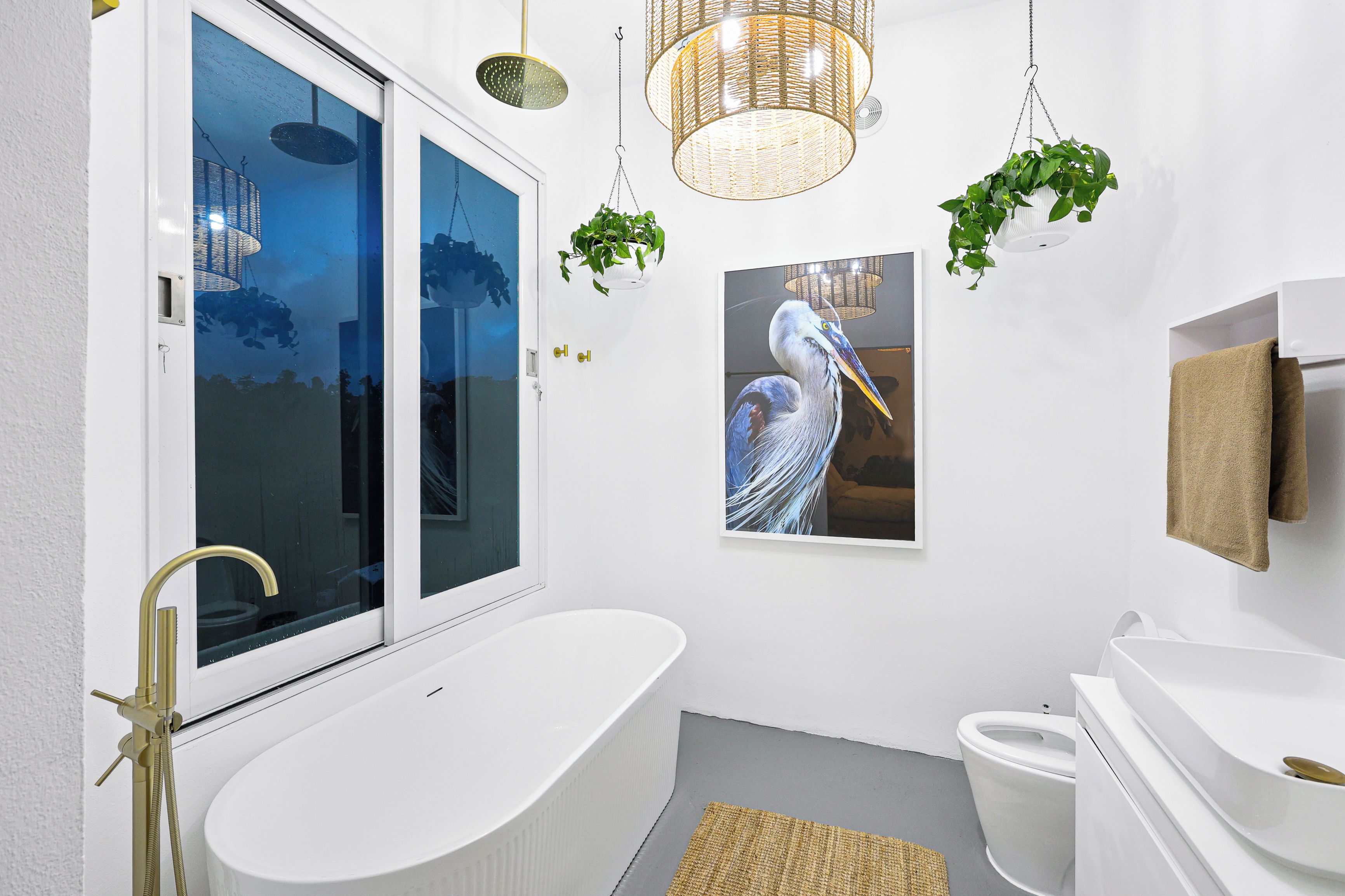 Ein modernes Badezimmer mit freistehender Badewanne, Toilette und Waschbecken. Hängende Pflanzen und ein großes Fenster mit Blick auf die Stadtlandschaft.