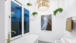Ein modernes Badezimmer mit freistehender Badewanne, Toilette und Waschbecken. Hängende Pflanzen und ein großes Fenster mit Blick auf die Stadtlandschaft.