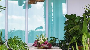 Ein Zimmer mit Tisch, Stühlen, hängenden Korblampen und großen Fenstern mit Vorhängen.
