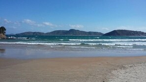 Une plage avec des vagues, un ciel dégagé et des montagnes à l’horizon.