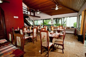 Un restaurante con varias mesas y sillas, una escalera y grandes ventanales.