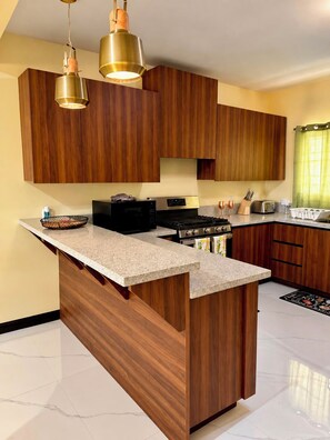 A modern kitchen with wooden cabinets, a central island, stainless steel appliances, and pendant lighting.