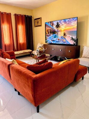 A living room with a large flat-screen TV, a sofa, a bench, and a cabinet. - Escape to Paradise!| Your Home Away From Home in Jamaica (Runaway bay)
