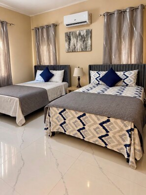 A hotel room with two beds, a wall-mounted air conditioner, and a painting.