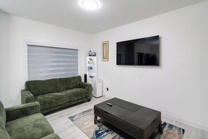 A living room with a green sofa, a black coffee table, a flat-screen TV, and a window with blinds. - Cozy Spacious 3-Bedroom Duplex in Cy Becker. (Edmonton)