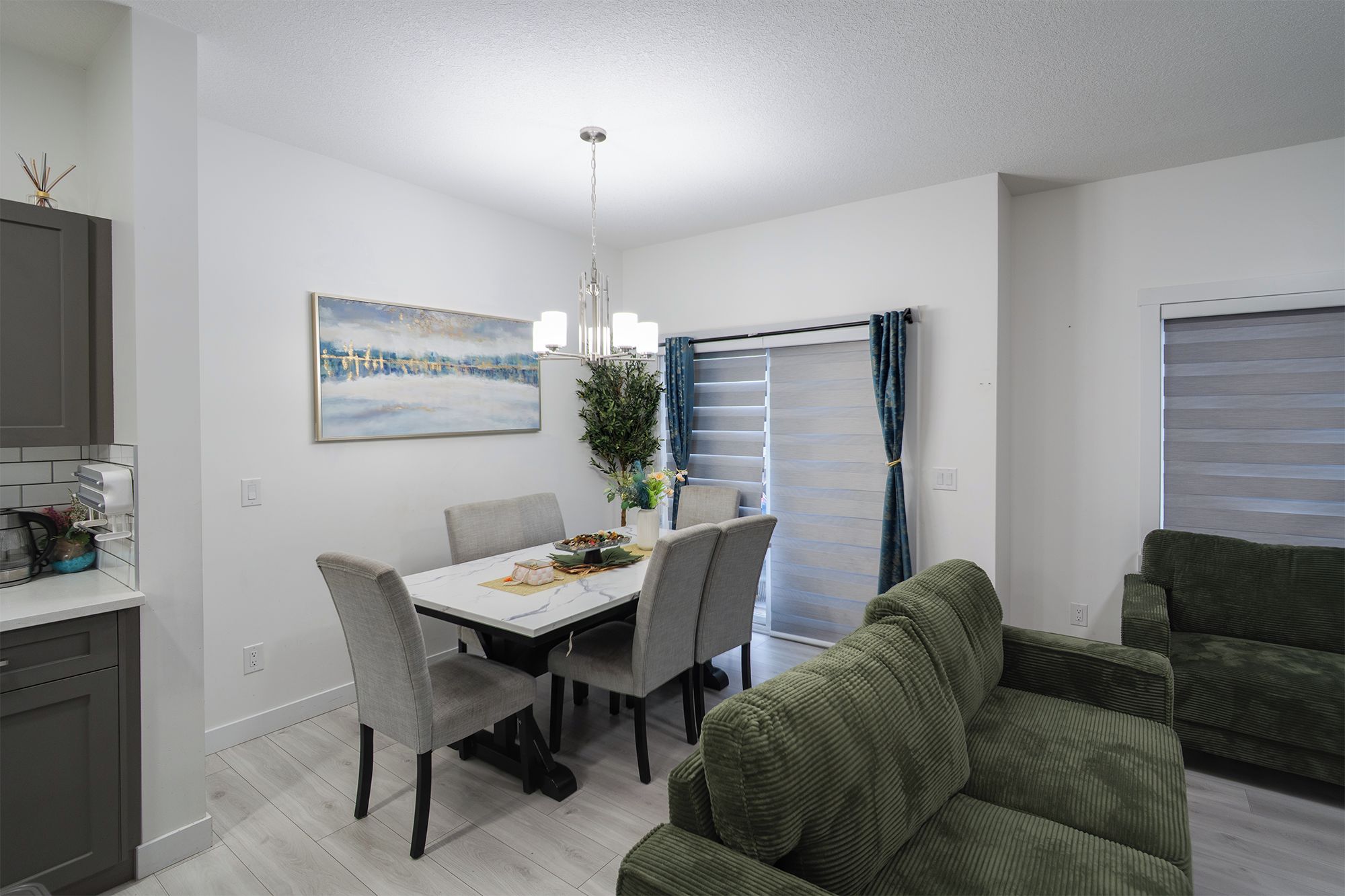 A dining area with a table, chairs, a chandelier, a painting, and a green sofa.