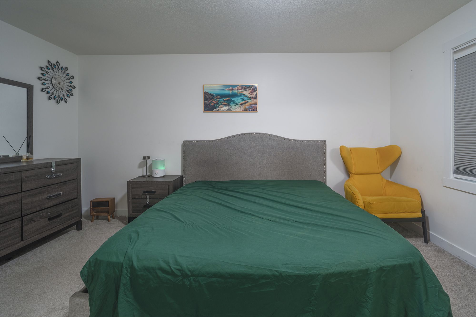A bedroom with a bed, a nightstand, a lamp, a chair, a painting, and a window.
