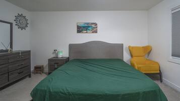 A bedroom with a bed, a nightstand, a lamp, a chair, a painting, and a window.