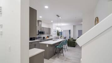 A modern kitchen with a central island, bar stools, and a dining area with a sofa.