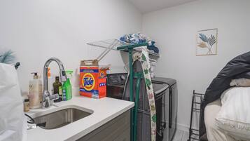 A compact kitchen with a sink, a drying rack, and a box of Tide detergent.