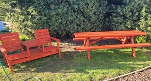 A picnic table and bench set in a garden with a hedge in the background.