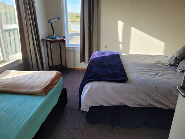 A bedroom with a bed, a small table with a lamp, a window with curtains, and a view of the outside.