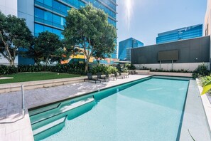 Ein Schwimmbecken mit Liegestühlen, umgeben von Grünflächen und modernen Gebäuden.
