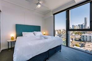 Ein Hotelzimmer mit einem großen Bett, zwei Nachttischlampen, Blick auf die Stadt und einem Deckenventilator.