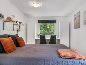 Una camera da letto con un letto, due poltrone, una finestra vista verde e uno scaffale con oggetti decorativi.