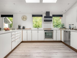 A modern kitchen with white cabinetry, a built-in oven, and a large window with a view of greenery. - "Nanook" -  from the sea by Interhome (Hadsund)