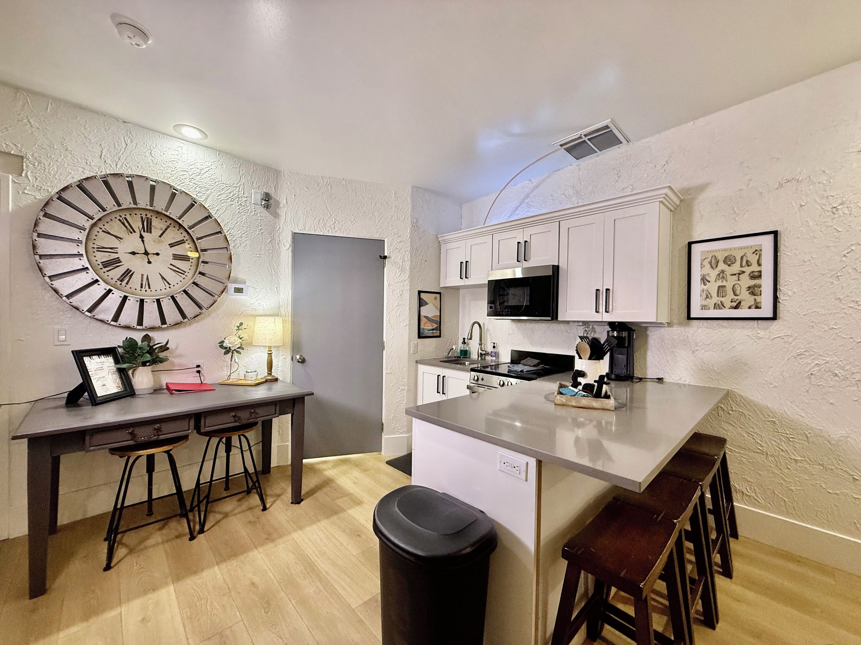 A modern kitchen with white cabinets, a large clock, and a bar area with stools.