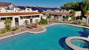 A swimming pool with a curved edge, surrounded by a white fence, and adjacent to a building with a red-tiled roof. - Tranquil Desert Retreat | Pools & Hot Tub (St George)
