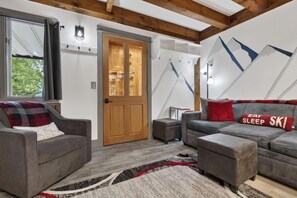 A modern living room with grey sofas, a wooden door, and a wall-mounted light fixture. - Riverbend Ski Retreat - Modern Condo minutes to Sunday River, Breweries & Bethel (Bethel)