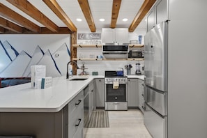 Une cuisine moderne dotée d’appareils électroménagers en acier inoxydable, de poutres en bois et d’un plan de travail blanc.