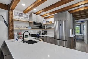 Cozinha moderna com ilha central, eletrodomésticos de aço inoxidável e vigas de madeira no teto.
