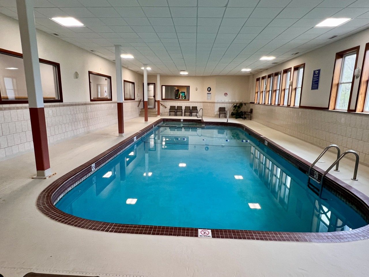 Una piscina interior con borde de azulejos, un cartel de 'No Diving' y una zona de estar con sillas.