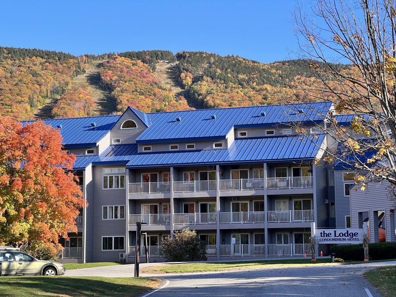A multi-story building with balconies, a sign indicating it's a condominium hotel, and a mountainous backdrop.