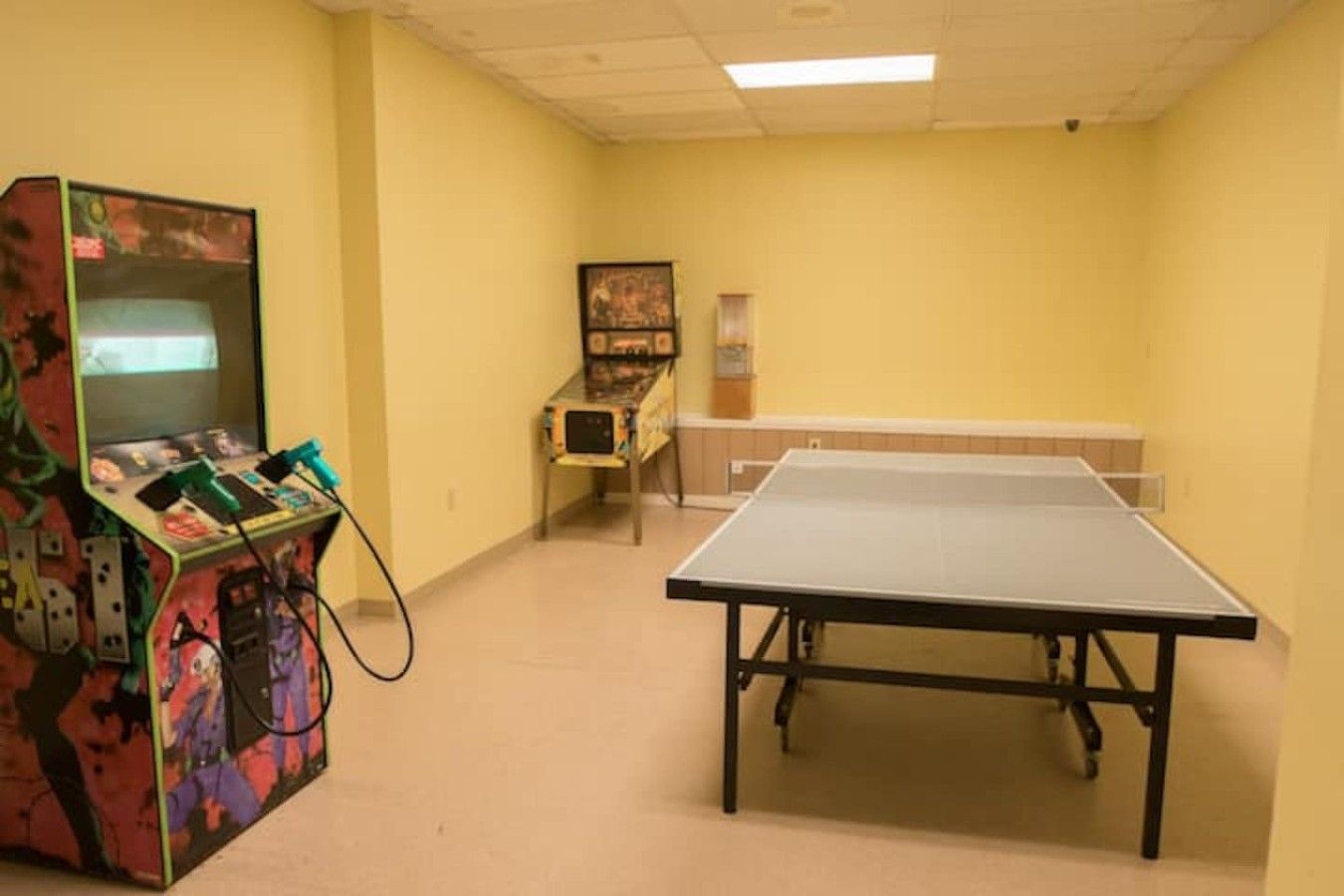 Quarto com mesa de pingue-pongue, console de jogos e uma pequena mesa com cadeira.