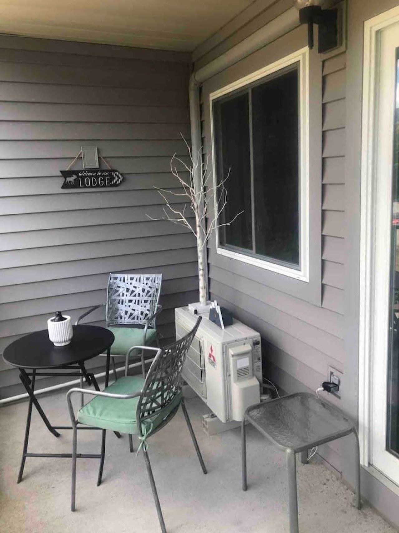 A porch with a table and chairs, a sign reading 'Welcome to our LODGE', and a large window.