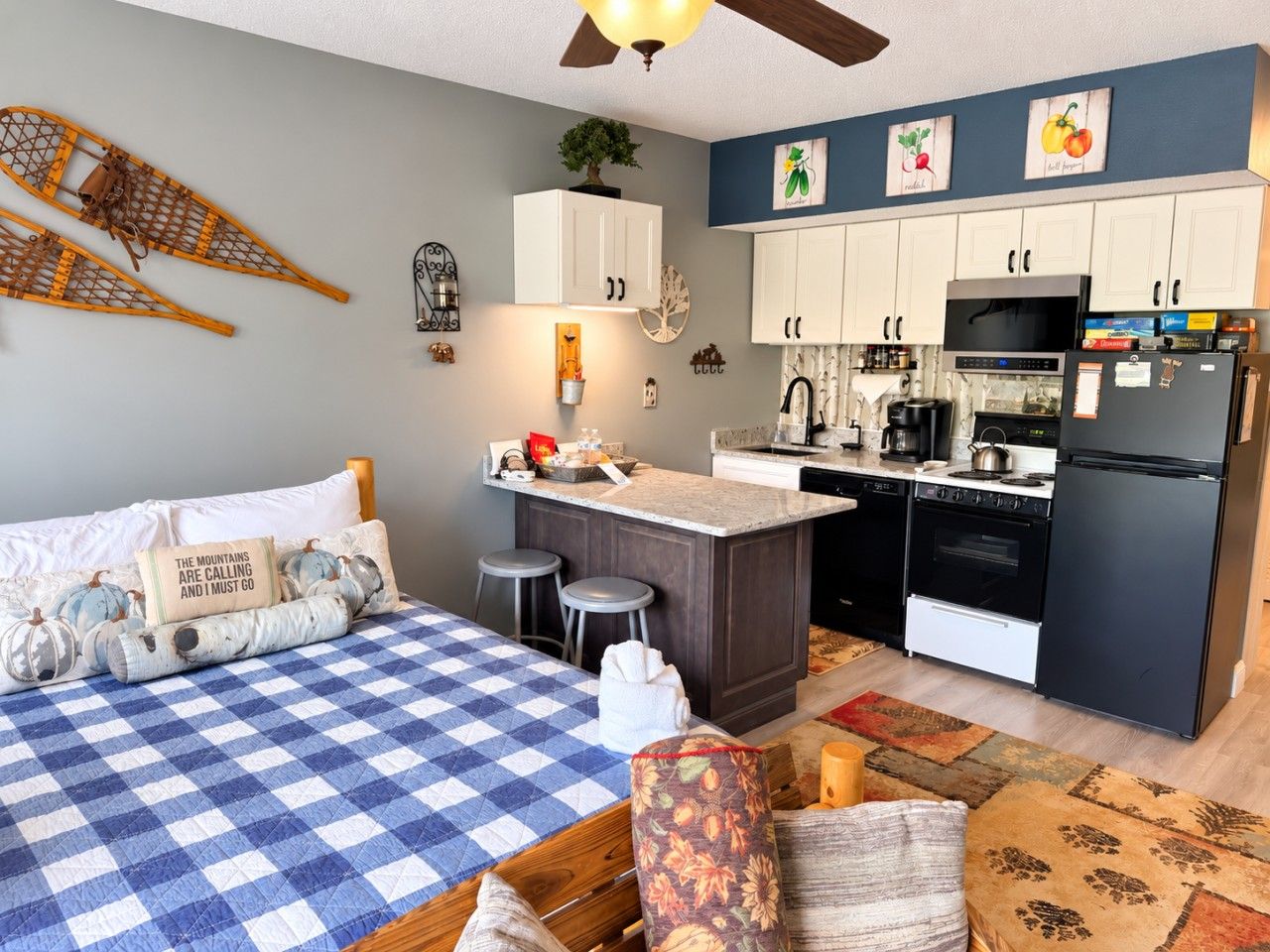 Cocina compacta con una isla central, comedor con mantel a cuadros y cama con almohadones decorativos.