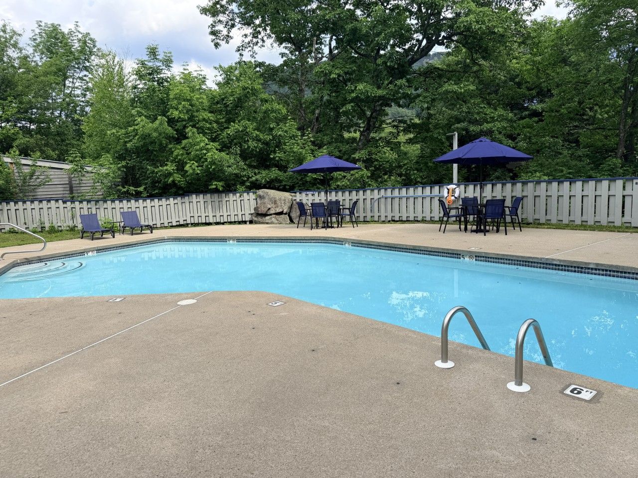 A swimming pool with a wooden fence, lounge chairs, and umbrellas.