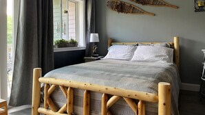 Quarto com cama de madeira, janela com cortinas, mesa de cabeceira com abajur e placa de patrulha de esqui fixada na parede.