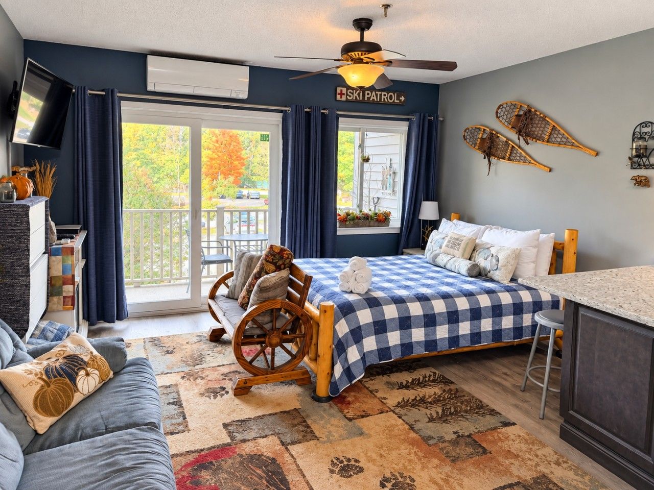 A hotel room with a bed, a wooden rocking chair, a desk, and a view of the outdoors.