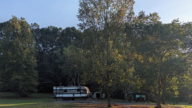 A gravel path leading to a white RV parked in a grassy area with trees in the background. - Reel Escape (Scottsboro)