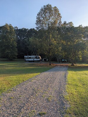 A gravel path leading to a white RV parked in a grassy area with trees in the background.