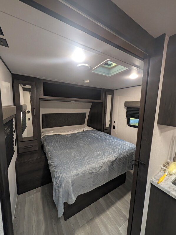 A compact bedroom with a bed, a small window, and a mirror.