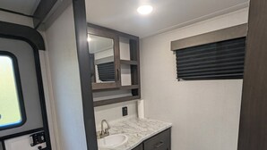 A compact bathroom with a sink, mirror, and toilet. - Reel Escape (Scottsboro)