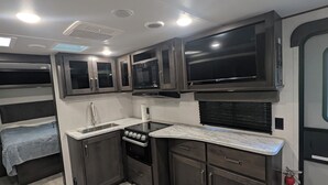 A compact kitchen with a stove, microwave, and cabinets, adjacent to a sleeping area with a bed. - Reel Escape (Scottsboro)