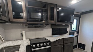 A kitchen with a built-in stove, microwave, and oven, with dark cabinetry and a marble countertop. - Reel Escape (Scottsboro)