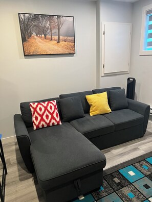 A modern living room with a sectional sofa, a patterned rug, and a framed landscape painting on the wall. - Brighton basement suite with 1 bedroom + sleeper sofa, peaceful and private. (Saskatoon)