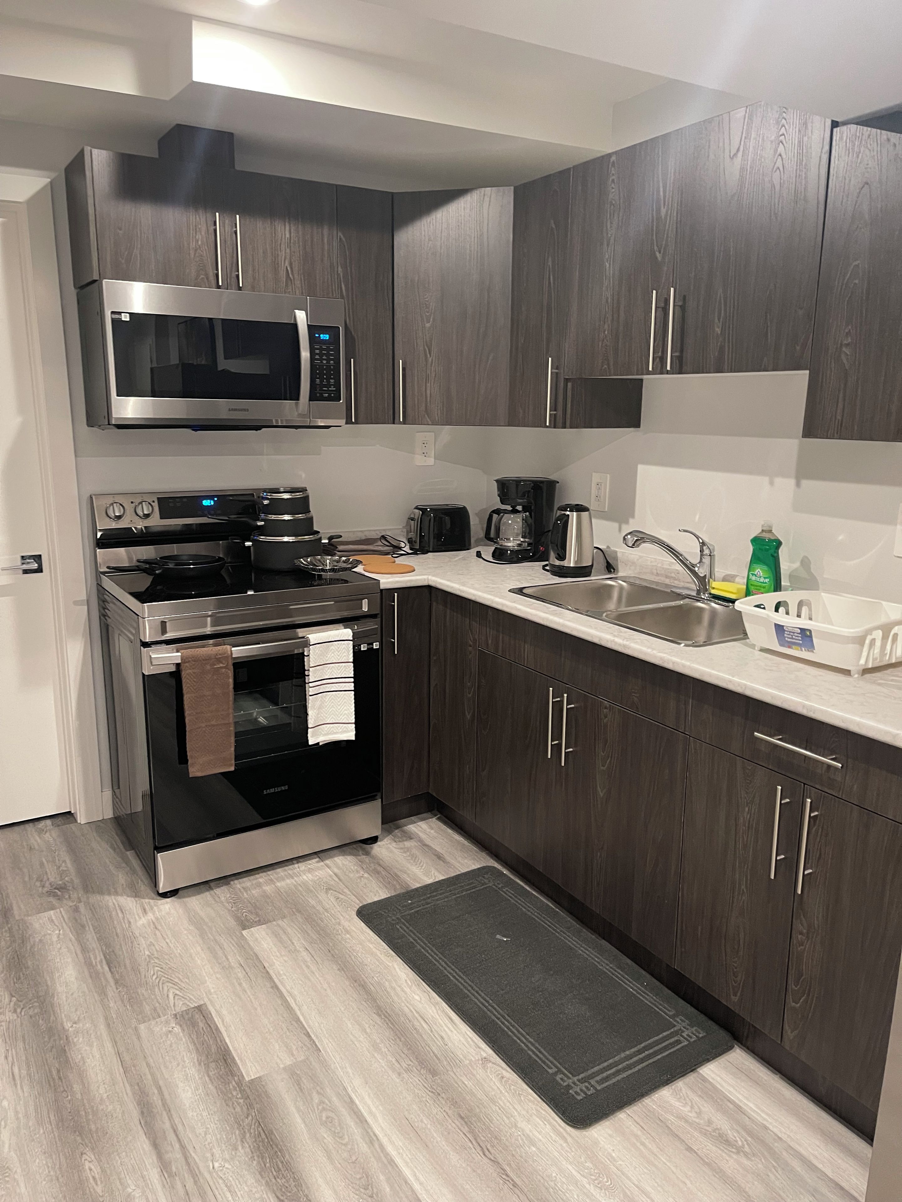 Eine moderne Küche mit dunklen Holzschränken, Edelstahlgeräten, einer Mikrowelle, einem Backofen und einer Kaffeemaschine.