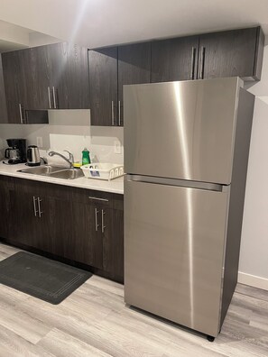 A modern kitchen with dark wood cabinets, stainless steel appliances, and a black mat on the floor. - Brighton basement suite with 1 bedroom + sleeper sofa, peaceful and private. (Saskatoon)