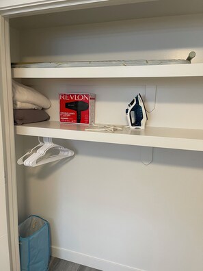 A closet with shelves containing a Revlon hair dryer, a blue plastic bag, and a white hanger. - Brighton basement suite with 1 bedroom + sleeper sofa, peaceful and private. (Saskatoon)